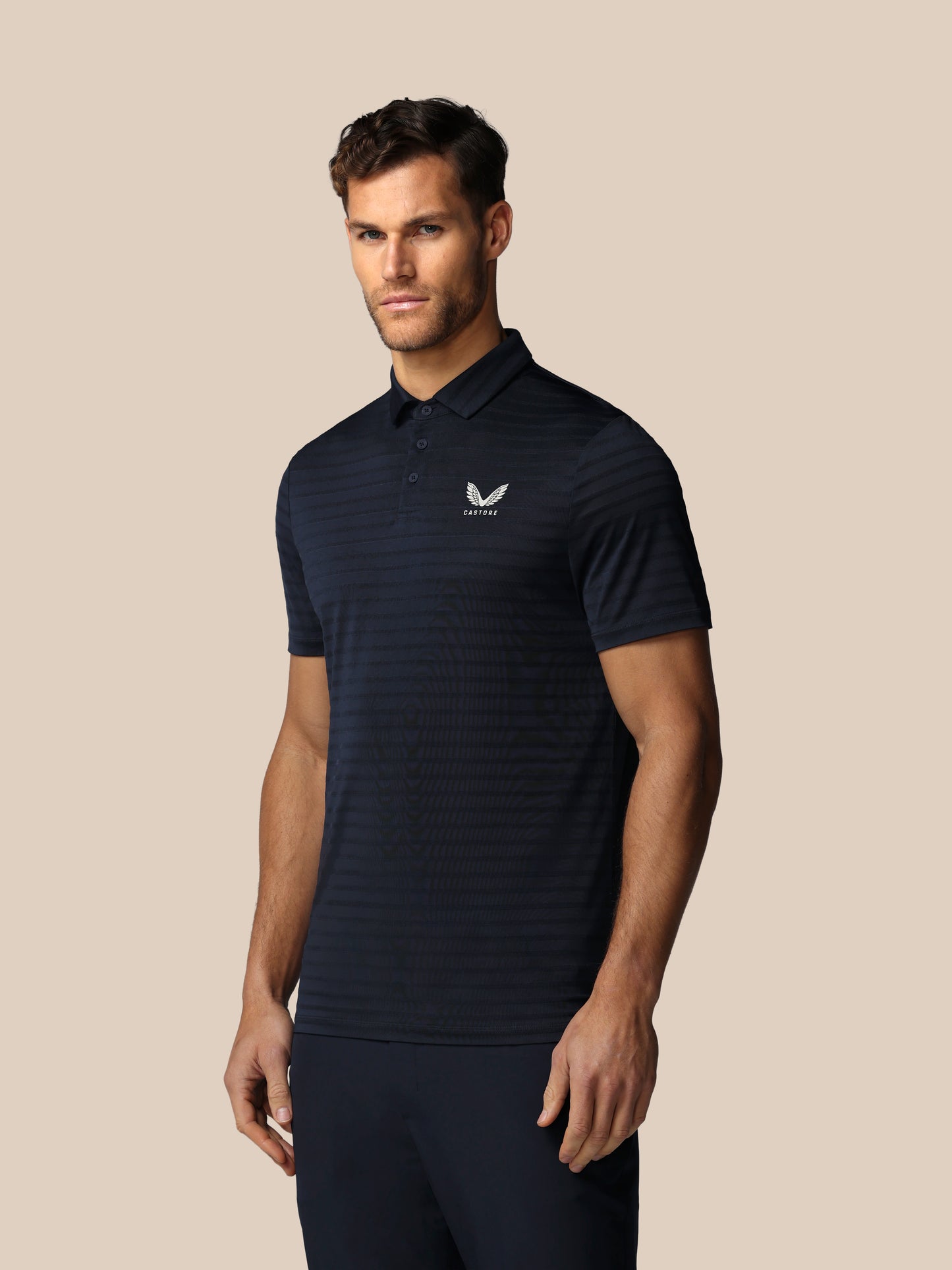 Man wearing a black striped polo shirt with a logo on a beige background