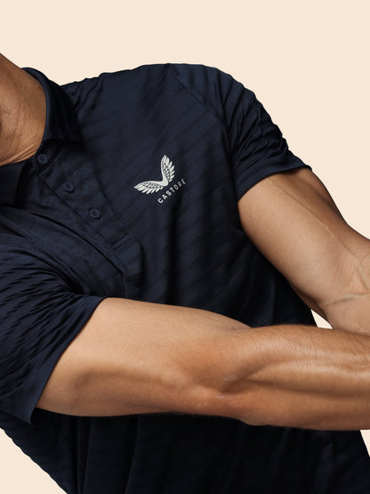 Person wearing a navy polo shirt with a logo on a beige background
