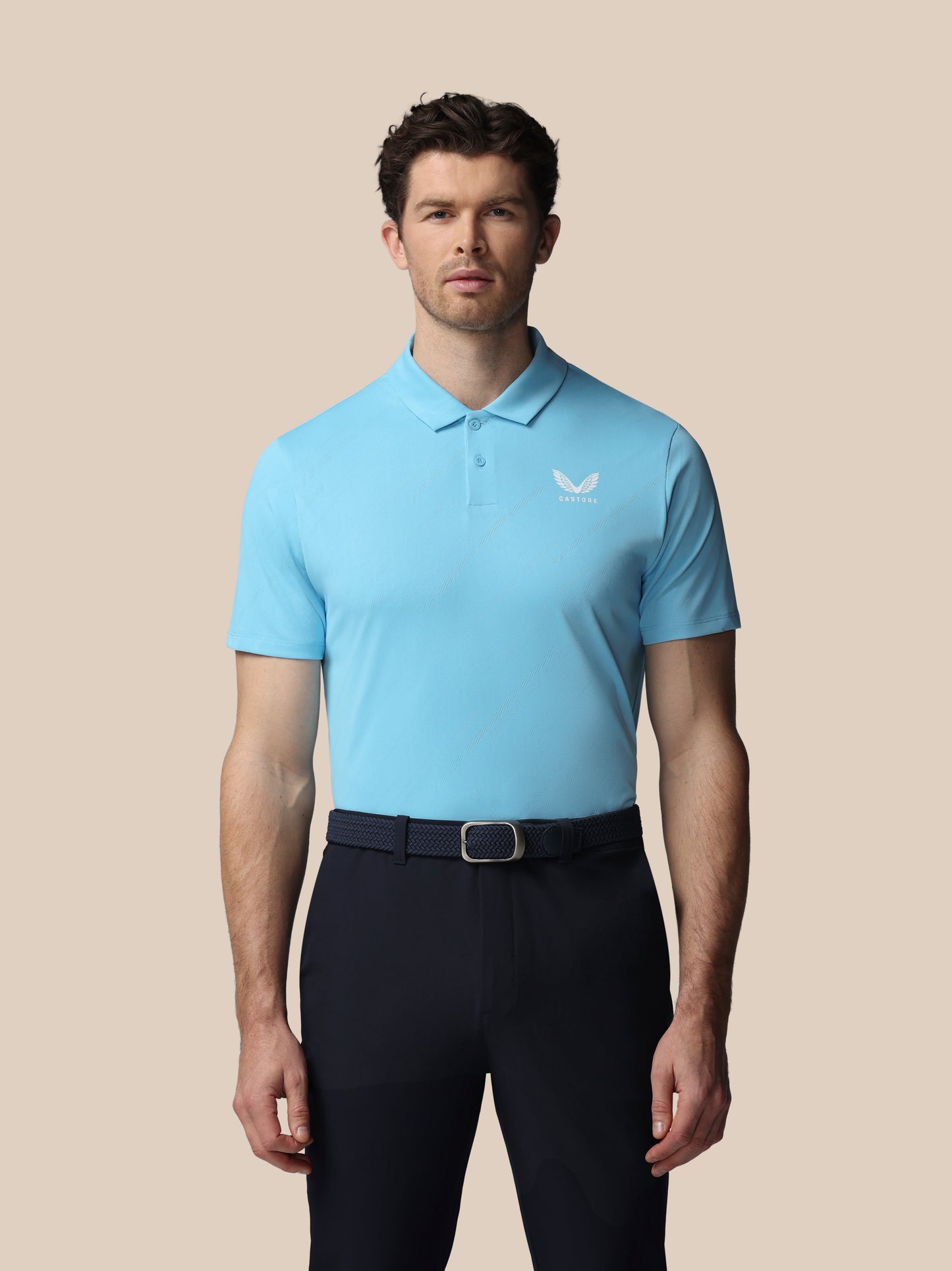 Man wearing a light blue polo shirt with a Castore logo on a beige background