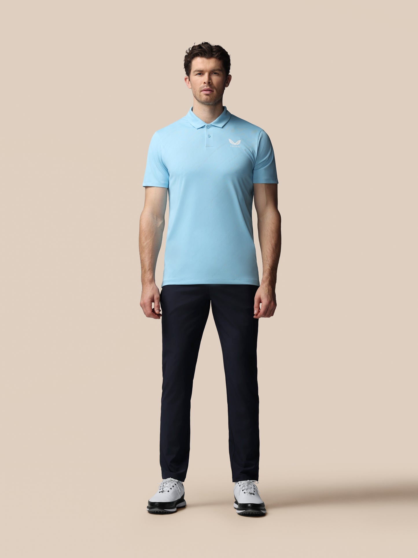 Man wearing a light blue polo shirt and black pants on a beige background