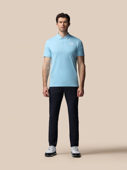 Man wearing a light blue polo shirt and black pants on a beige background