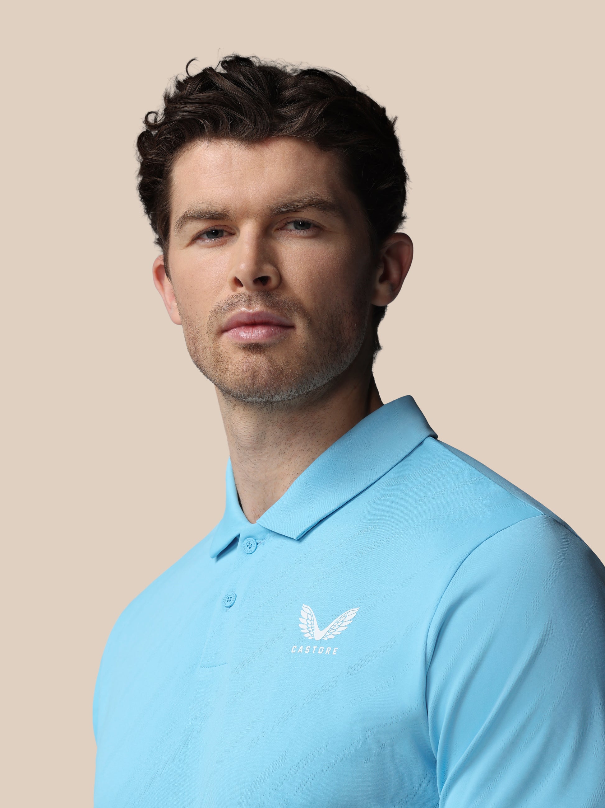 Man wearing a light blue polo shirt with a logo on a beige background