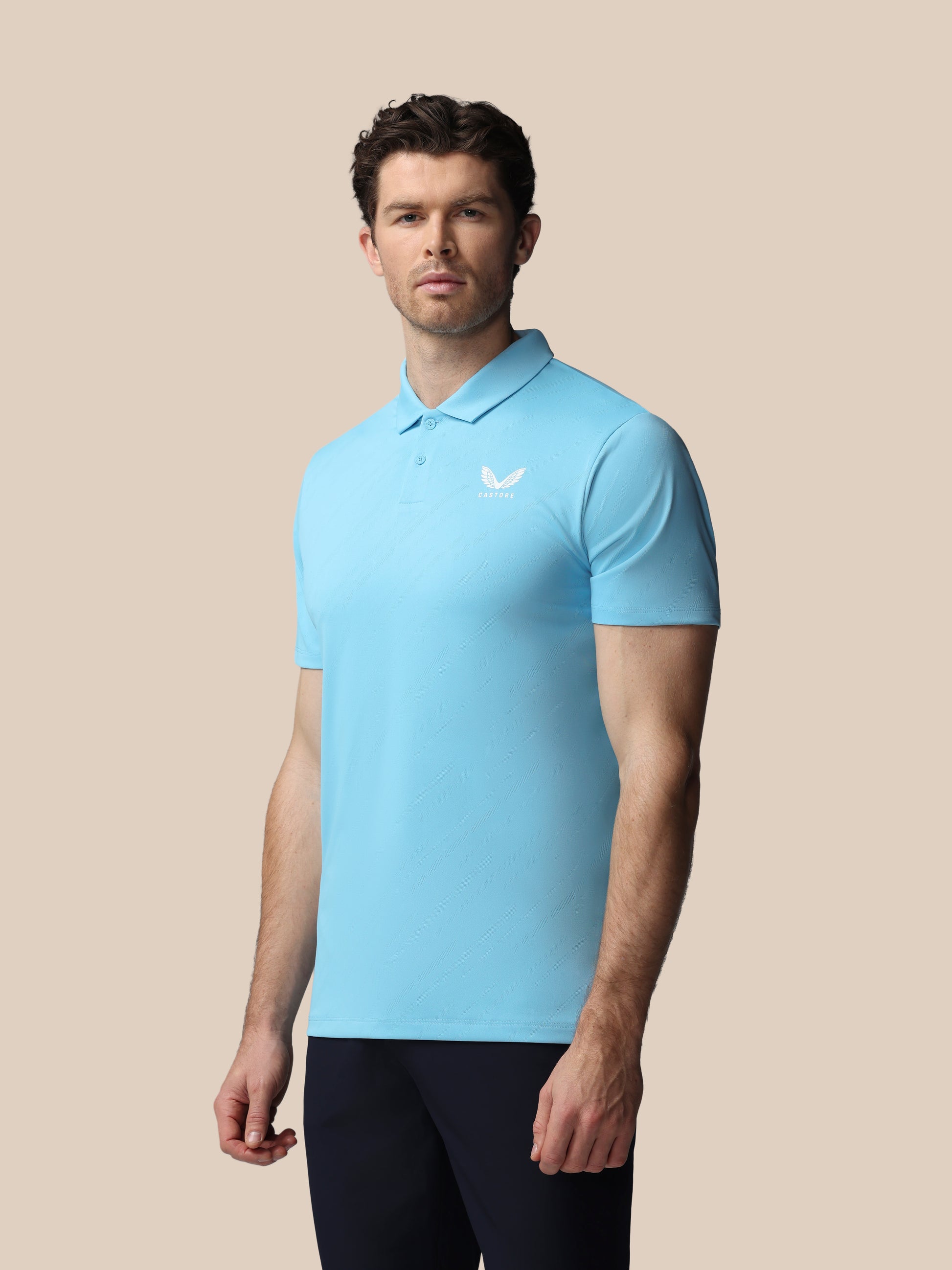 Man wearing a light blue polo shirt with a Castore logo on a beige background
