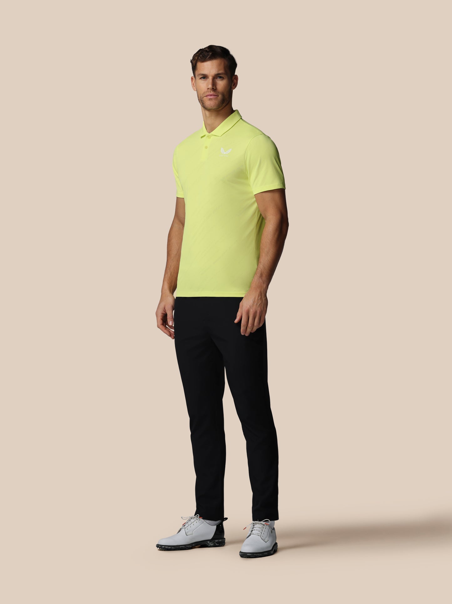 Man wearing a bright yellow polo shirt and black pants on a beige background