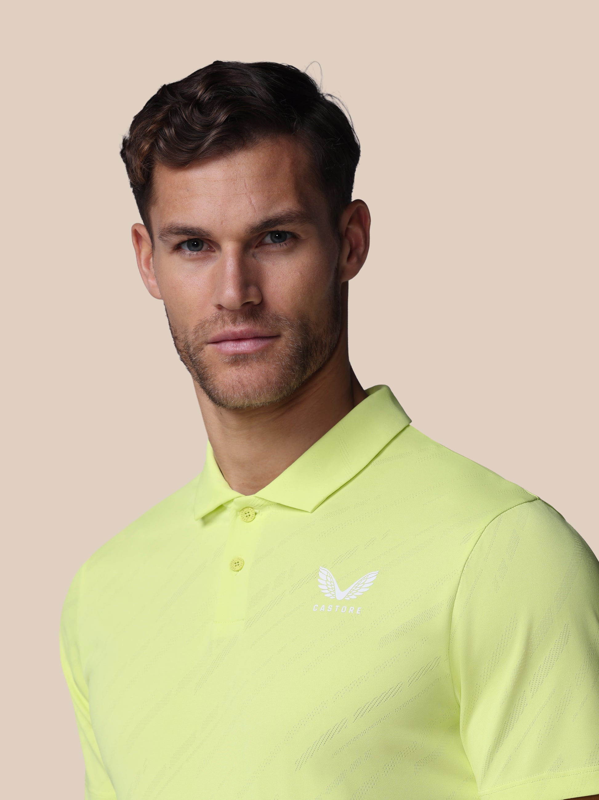 Man wearing a light green polo shirt with a brand logo on a beige background