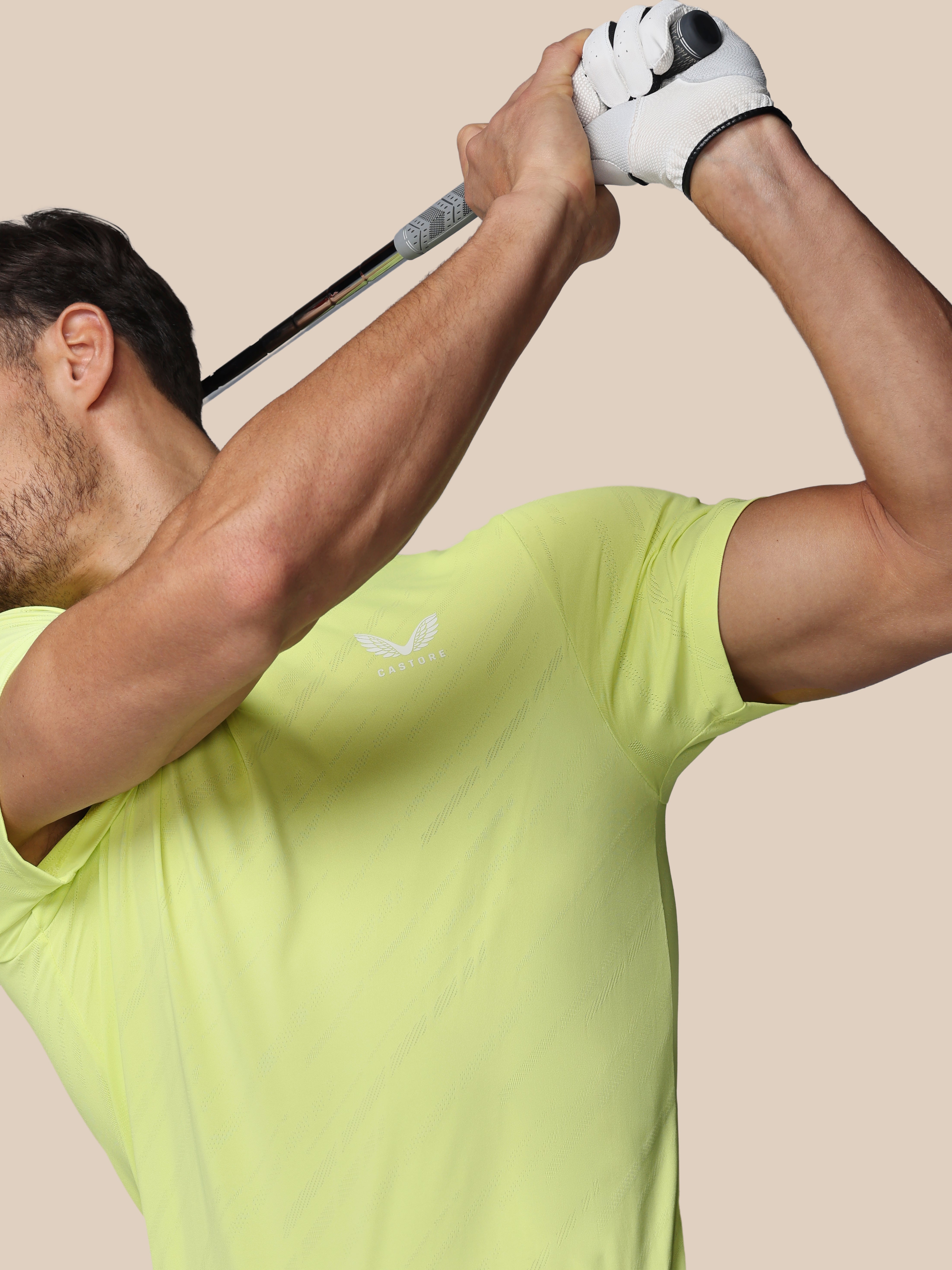 Man in a yellow shirt swinging a golf club against a beige background