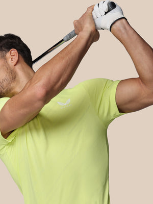 Man in a yellow shirt swinging a golf club against a beige background