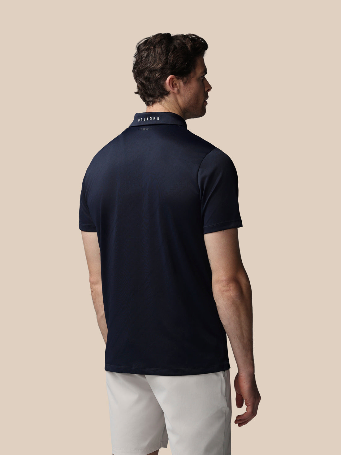 Man wearing a navy polo shirt with a visible brand logo on a beige background
