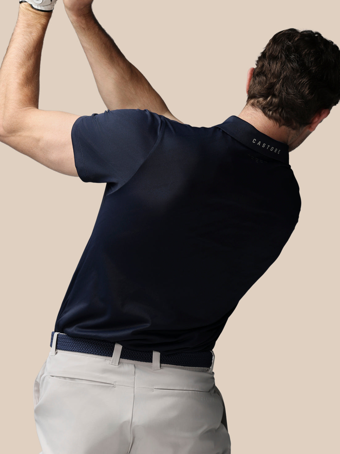 Man wearing a navy polo shirt with a visible brand logo, standing against a beige background.