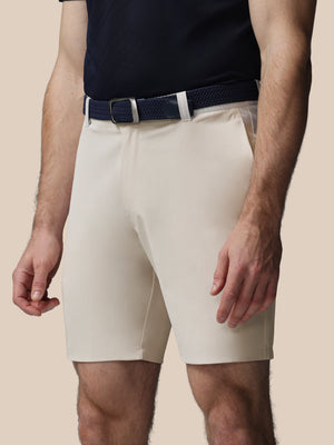 Person wearing beige shorts and a navy belt on a beige background