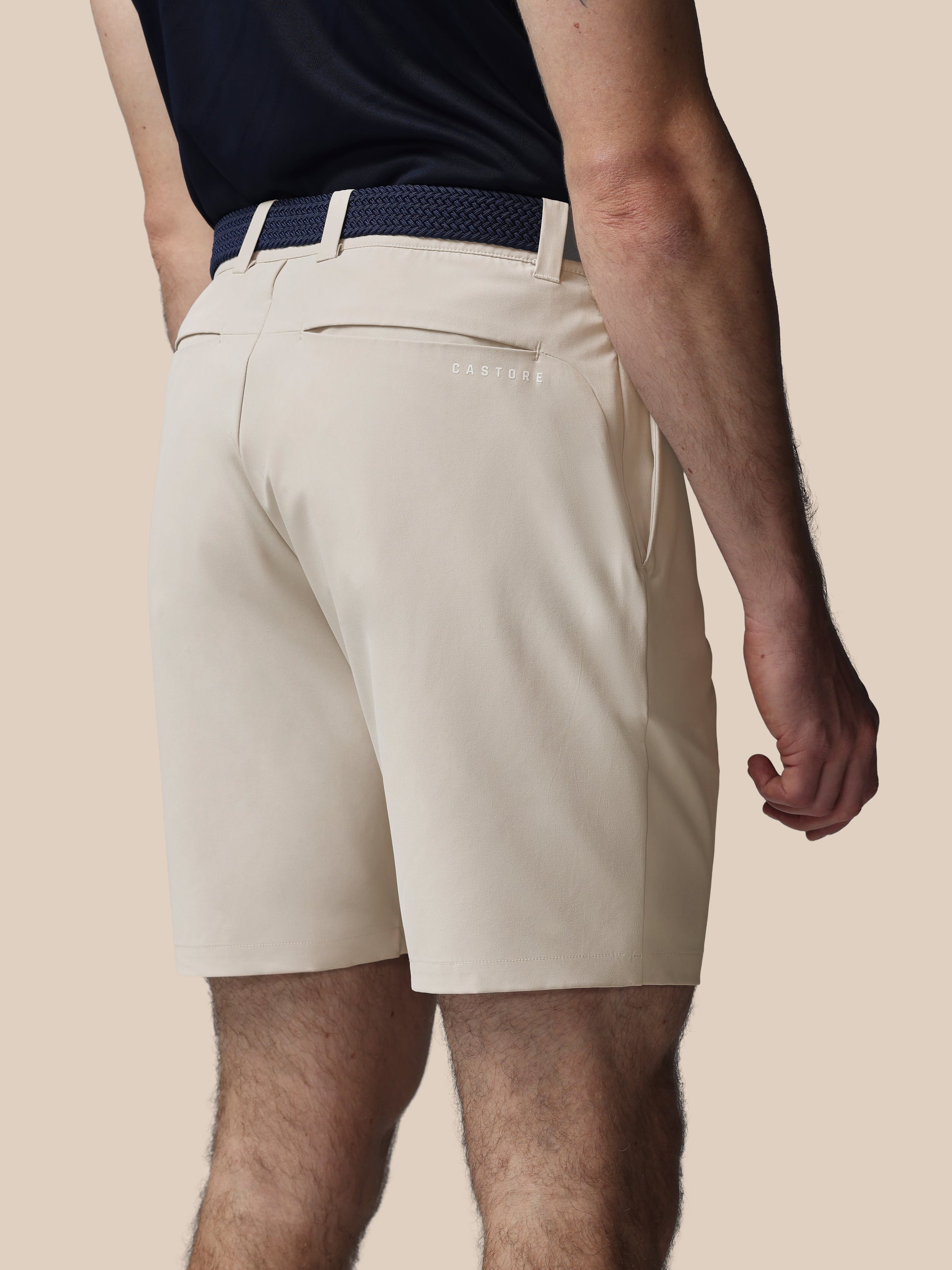 Person wearing beige shorts and a navy belt on a beige background