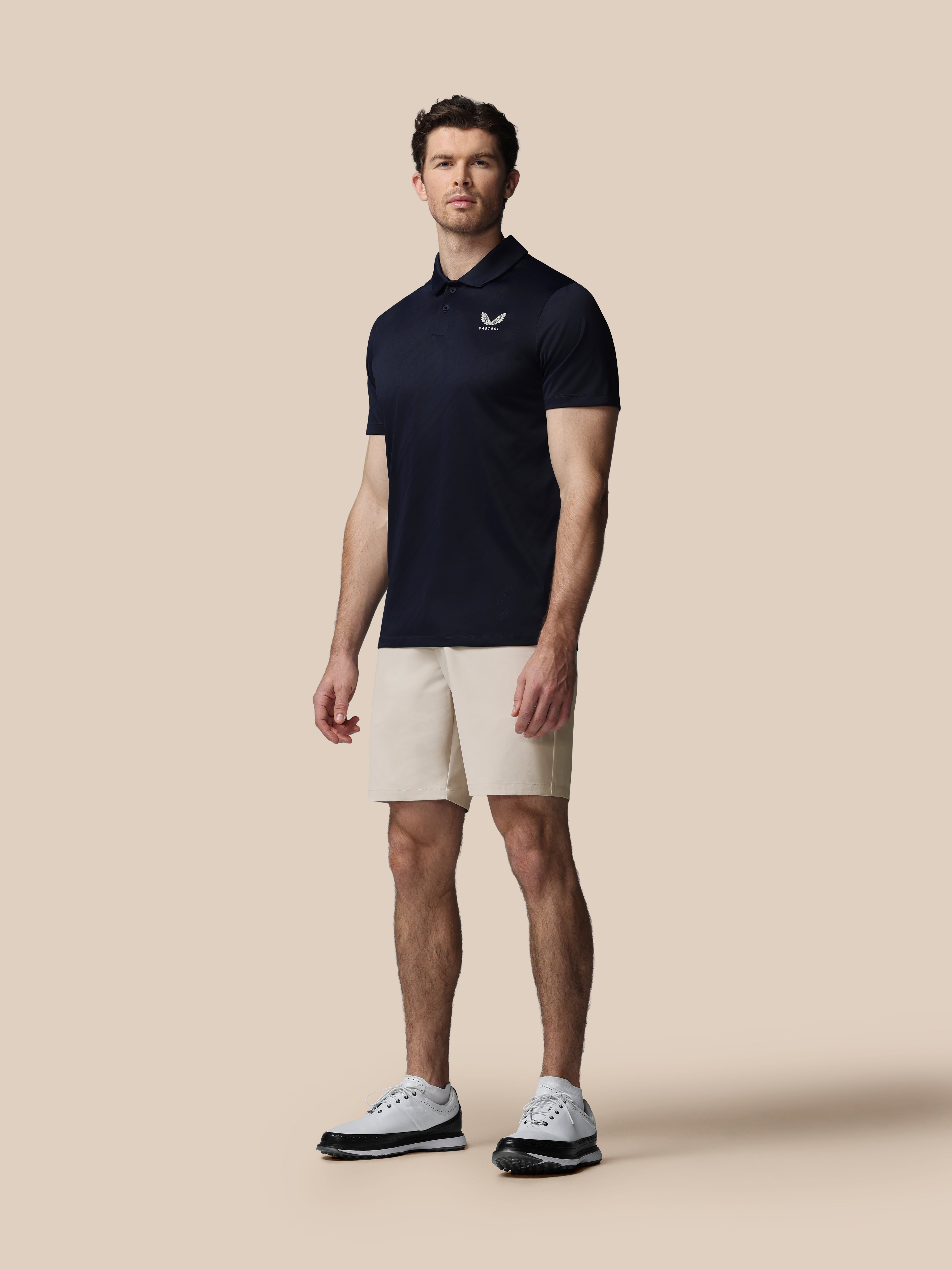 Man wearing a navy polo shirt and beige shorts on a beige background