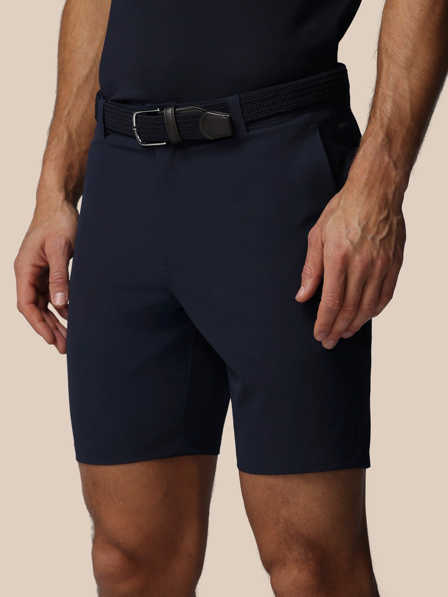 Person wearing navy shorts with a belt on a beige background