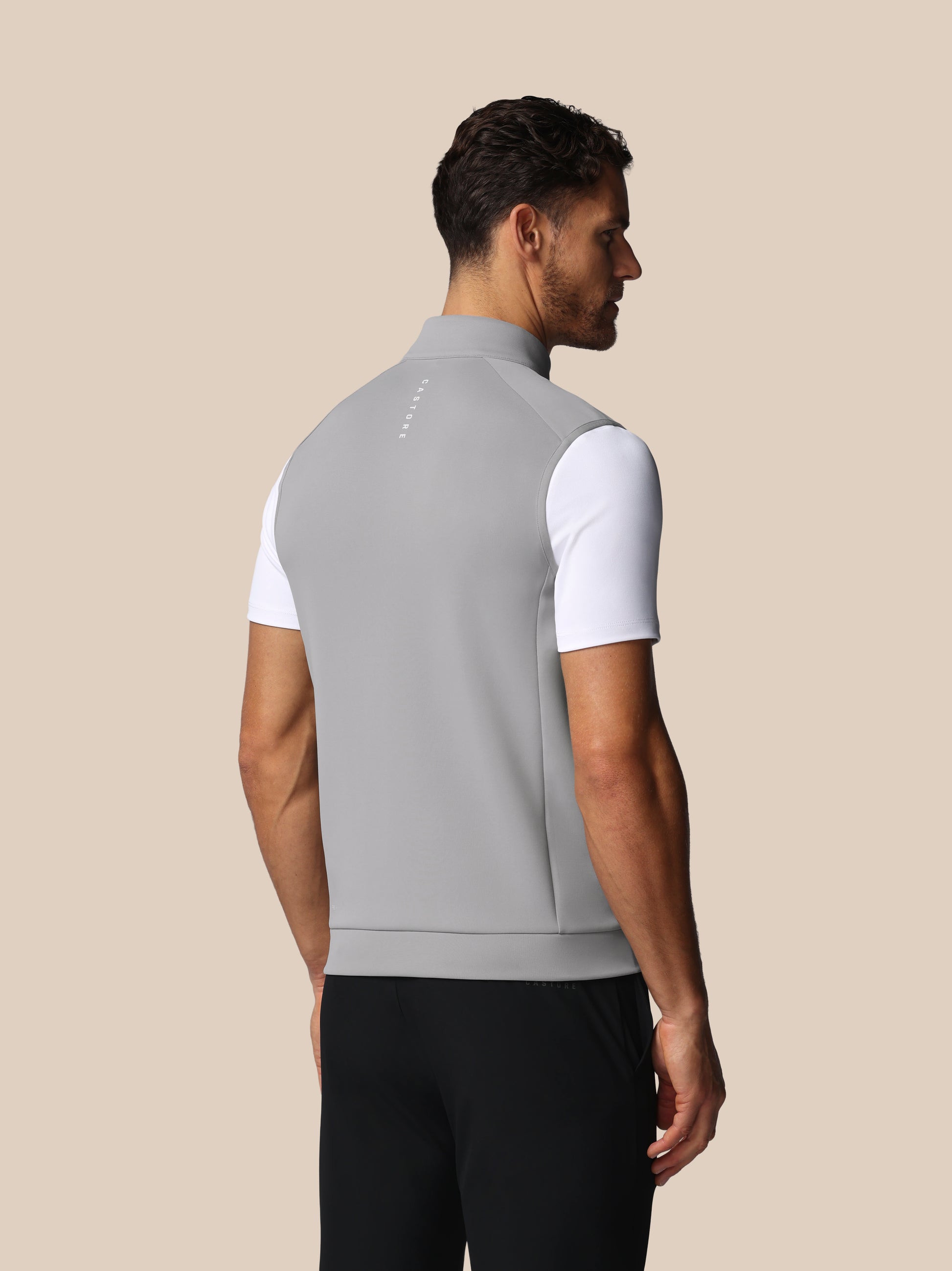 Man wearing a gray sleeveless jacket over a white shirt on a beige background