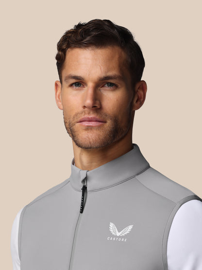 Man wearing a gray vest with a brand logo on a beige background