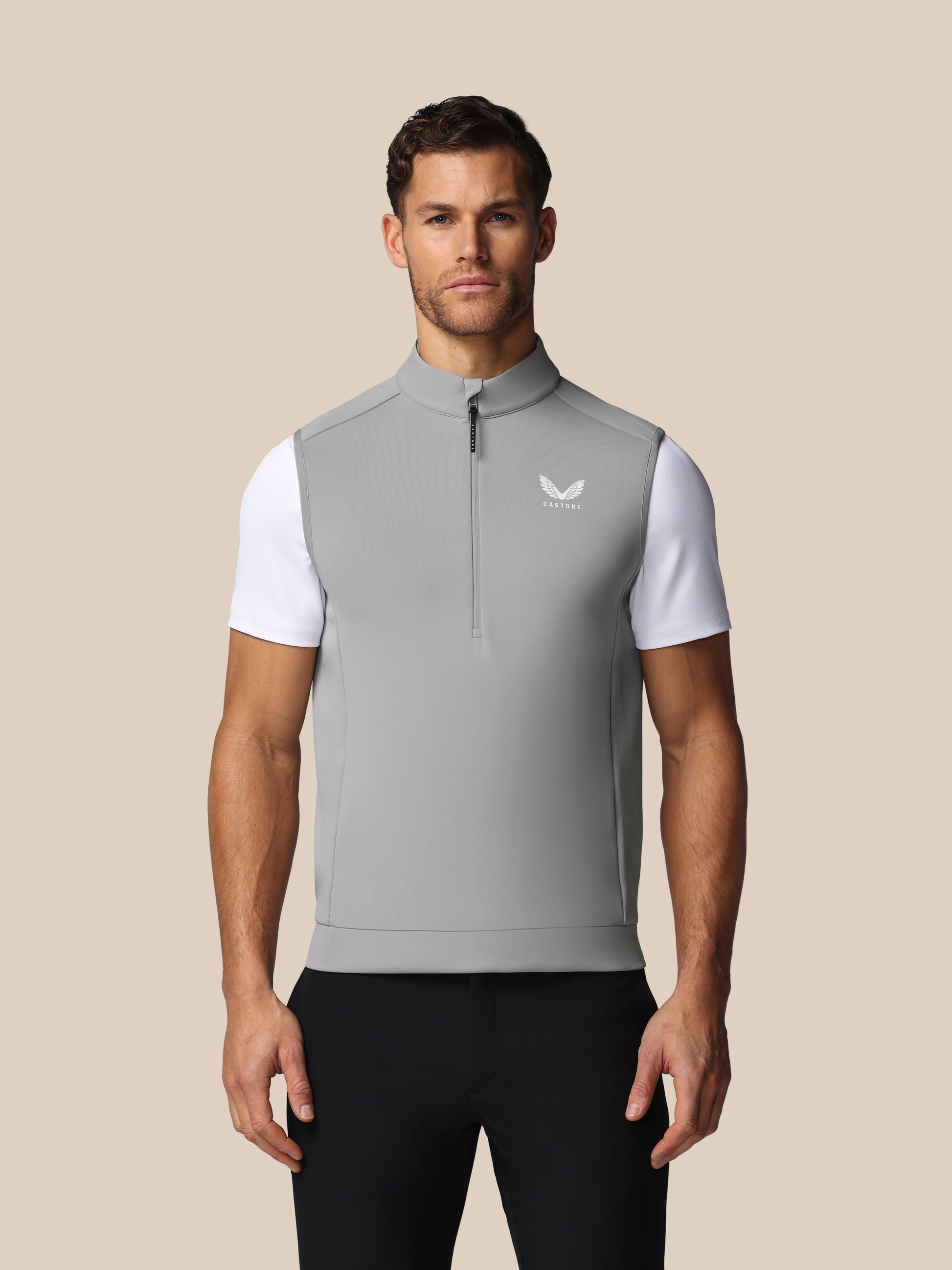 Man wearing a gray vest with a white logo on a beige background
