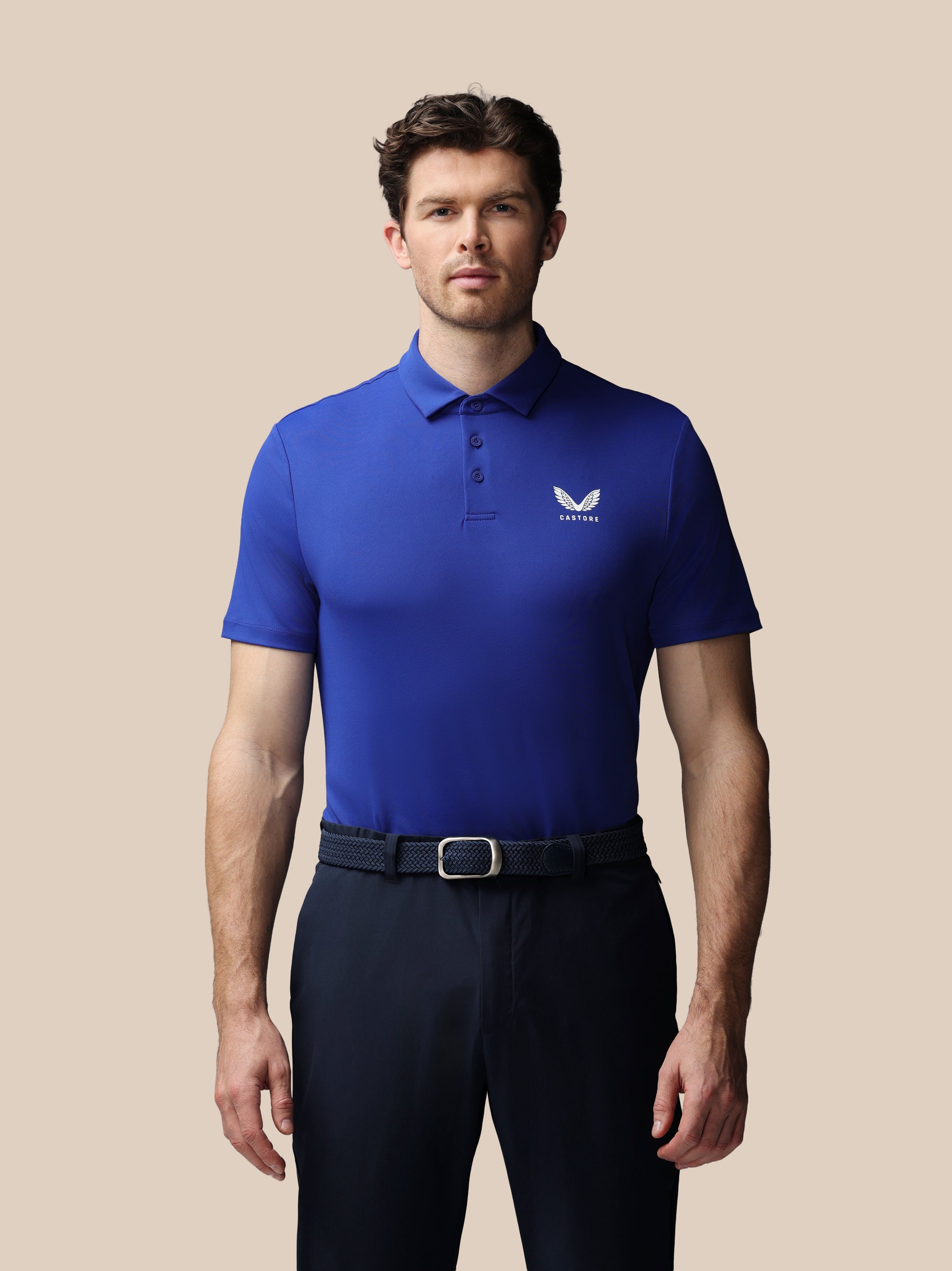 Man wearing a blue polo shirt with a logo on a beige background
