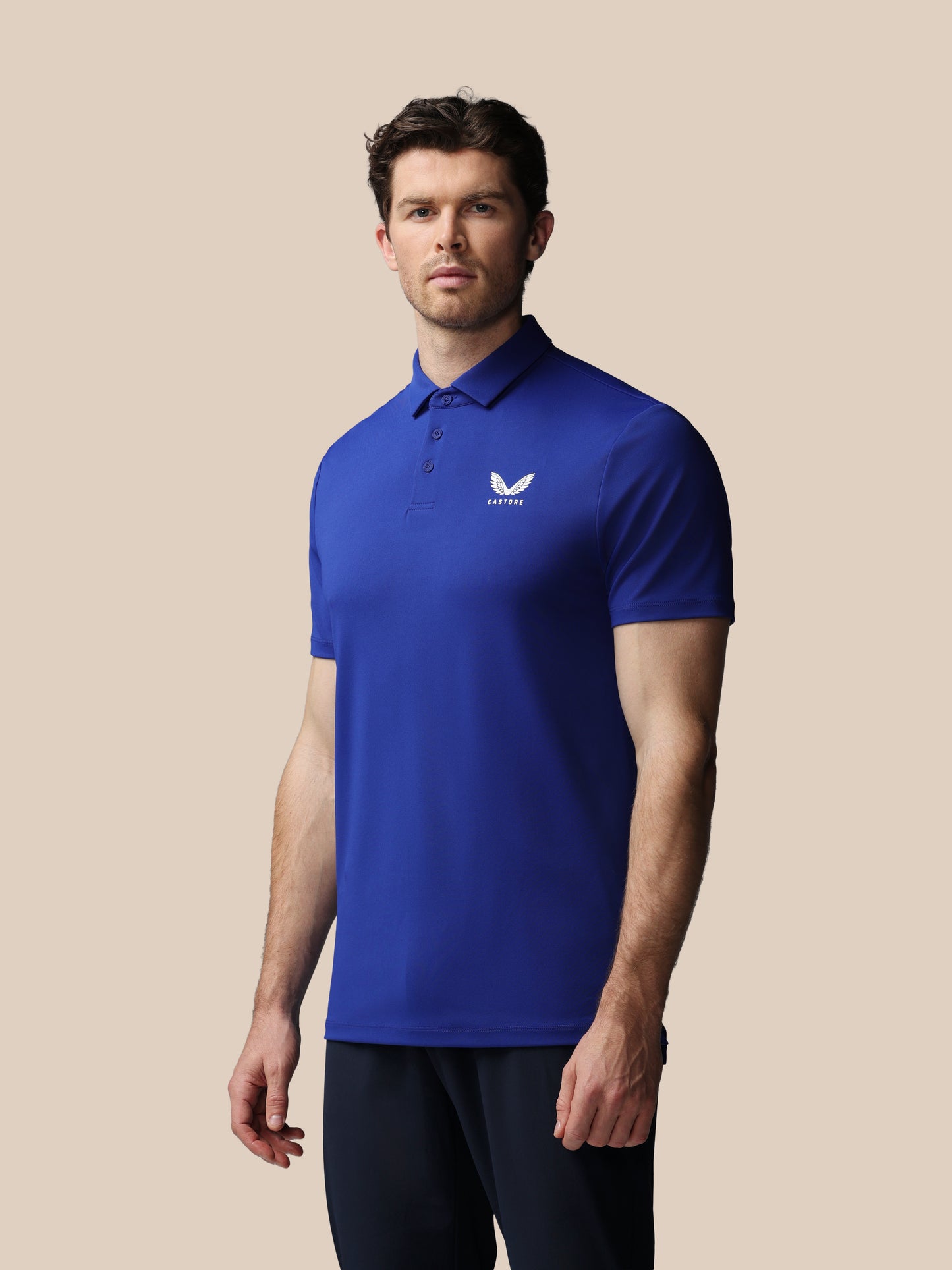 Man wearing a blue polo shirt with a Castore logo on a beige background