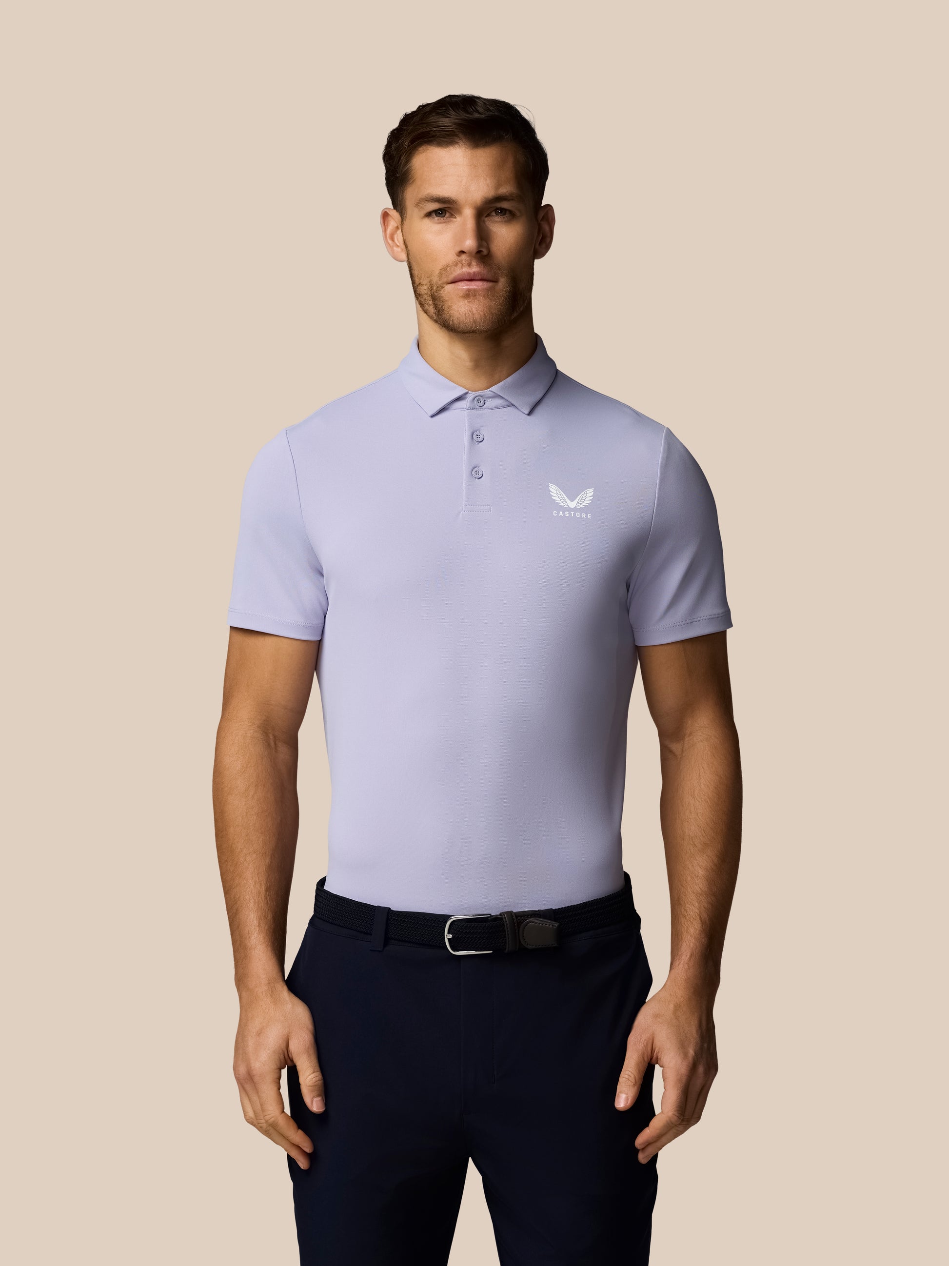 Man wearing a light purple polo shirt with a logo on a beige background
