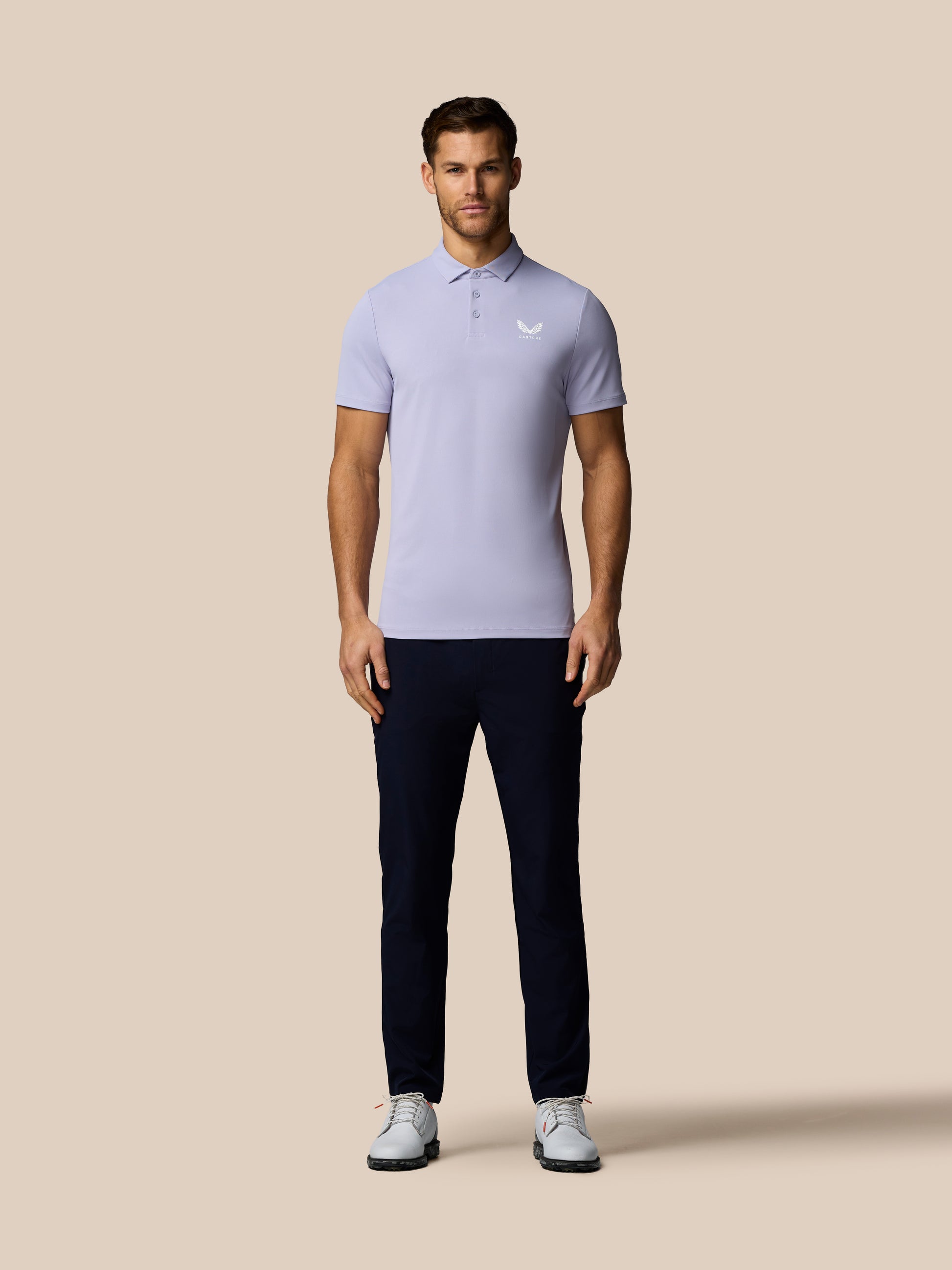 Man wearing a light purple polo shirt and dark pants on a beige background