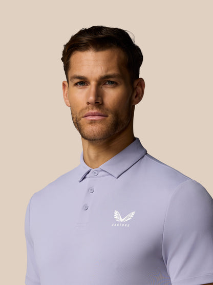 Man wearing a light purple polo shirt with a logo on a beige background