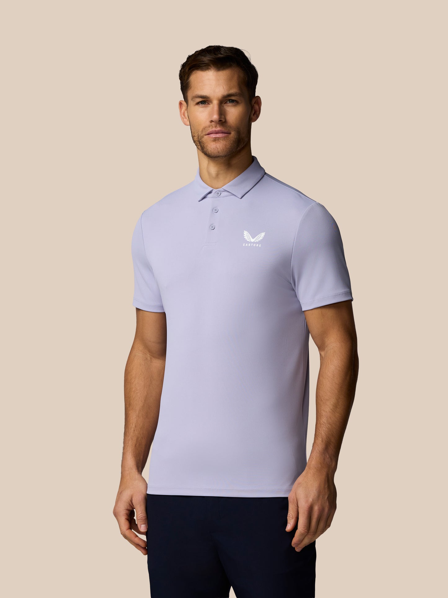 Man wearing a light purple polo shirt with a Castore logo on a beige background