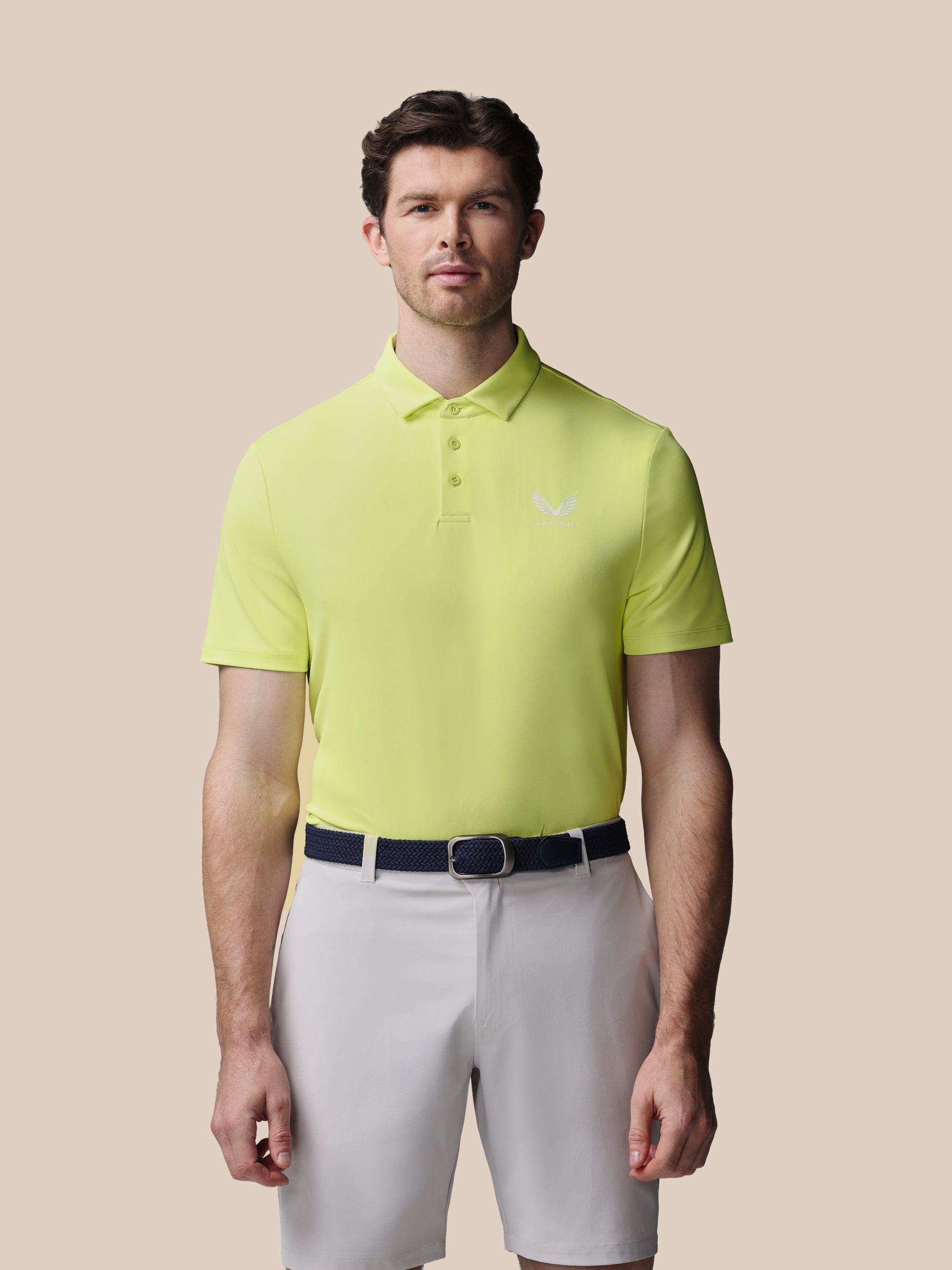 Man wearing a bright yellow polo shirt with the Castore logo on a beige background