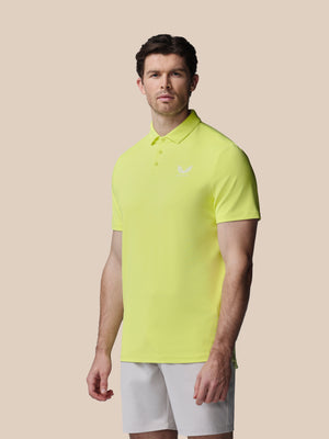 Man wearing a bright yellow polo shirt and white shorts on a beige background