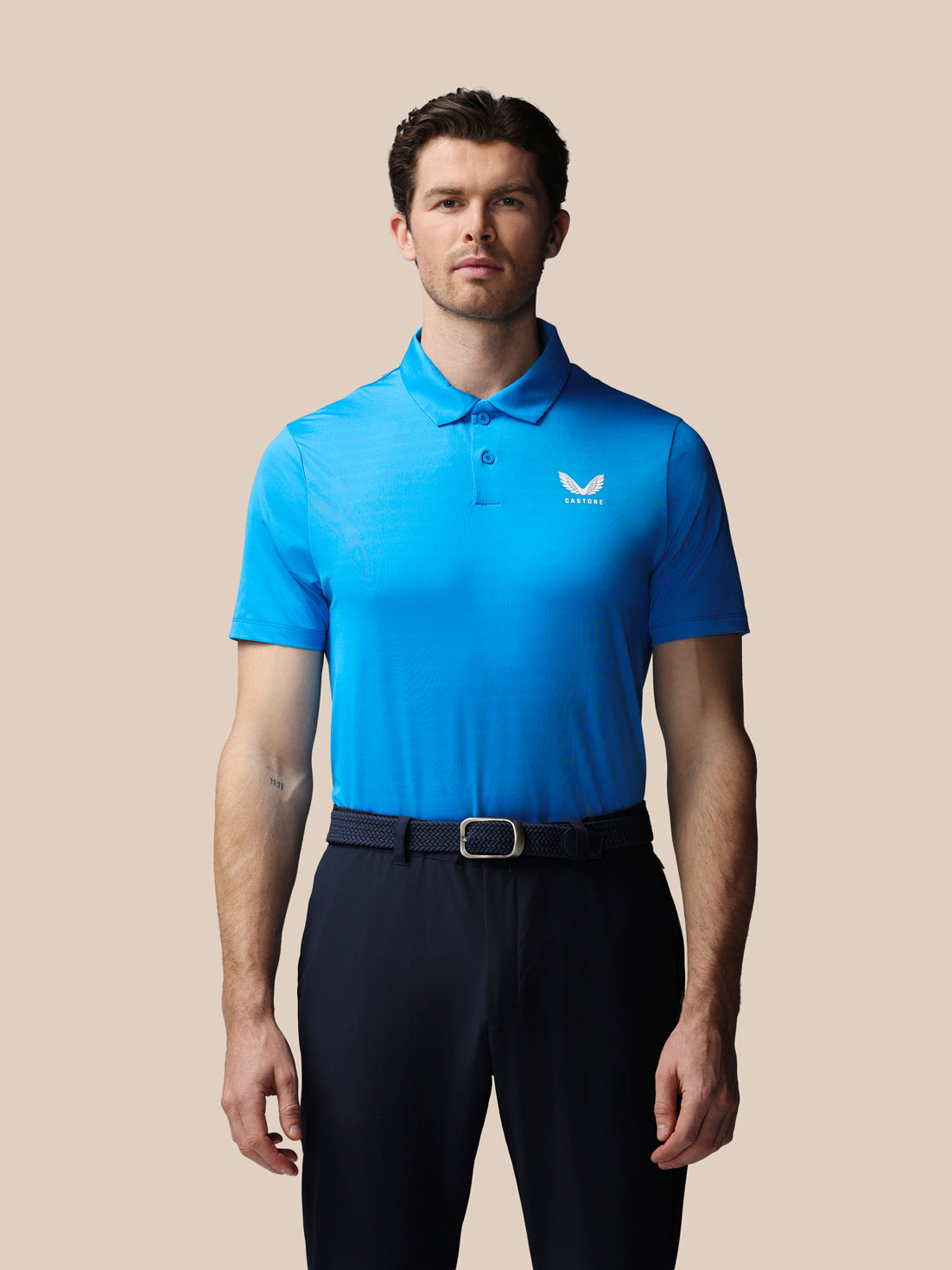 Man wearing a blue polo shirt with a logo on a beige background