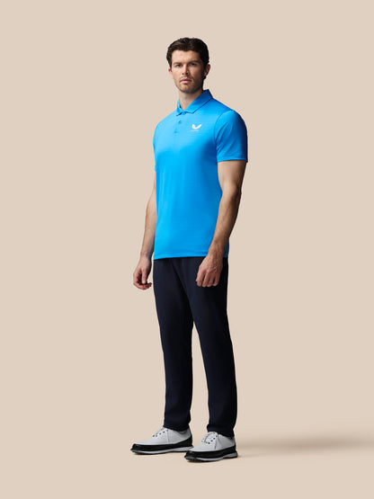 Man wearing a blue Castore polo shirt and black pants on a beige background