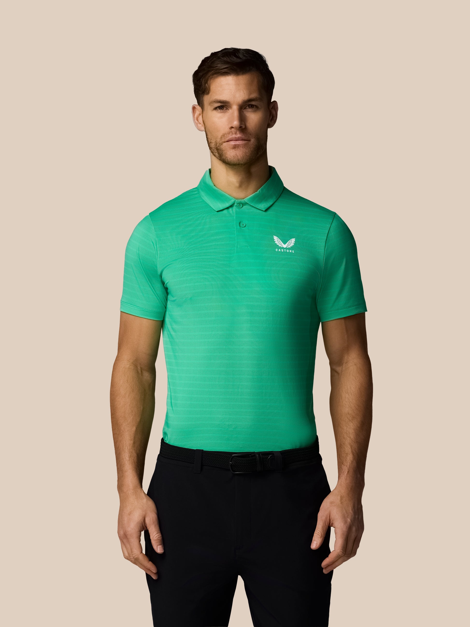 Man wearing a green striped polo shirt with Castore logo on a beige background