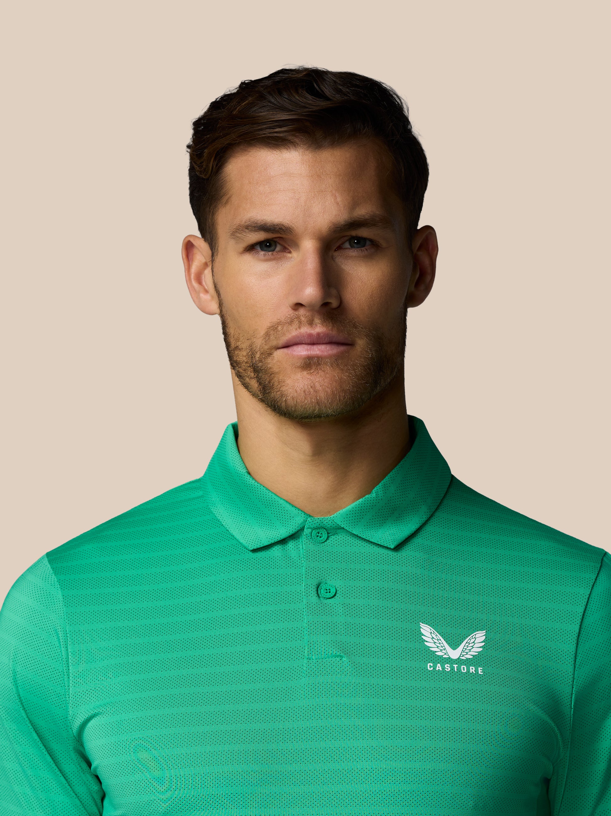 Man wearing a green polo shirt with a Castore logo on a beige background