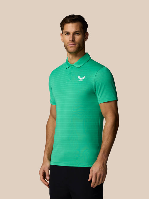 Man wearing a green striped polo shirt with Castore logo on a beige background