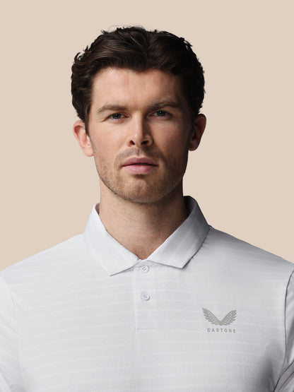 Man wearing a light gray polo shirt with a logo on a beige background