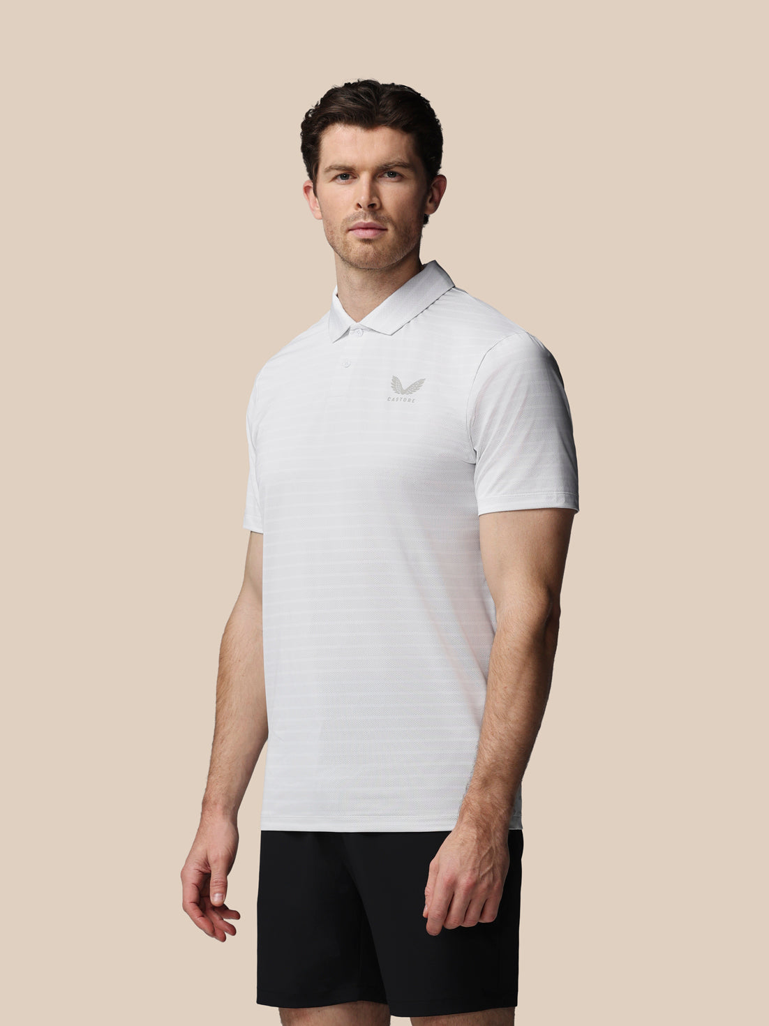Man wearing a white polo shirt with a logo on a beige background