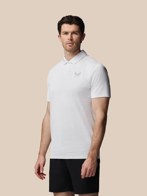 Man wearing a white polo shirt with a logo on a beige background
