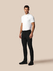 Man wearing a white polo shirt and black pants on a beige background