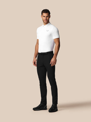Man wearing a white polo shirt and black pants on a beige background