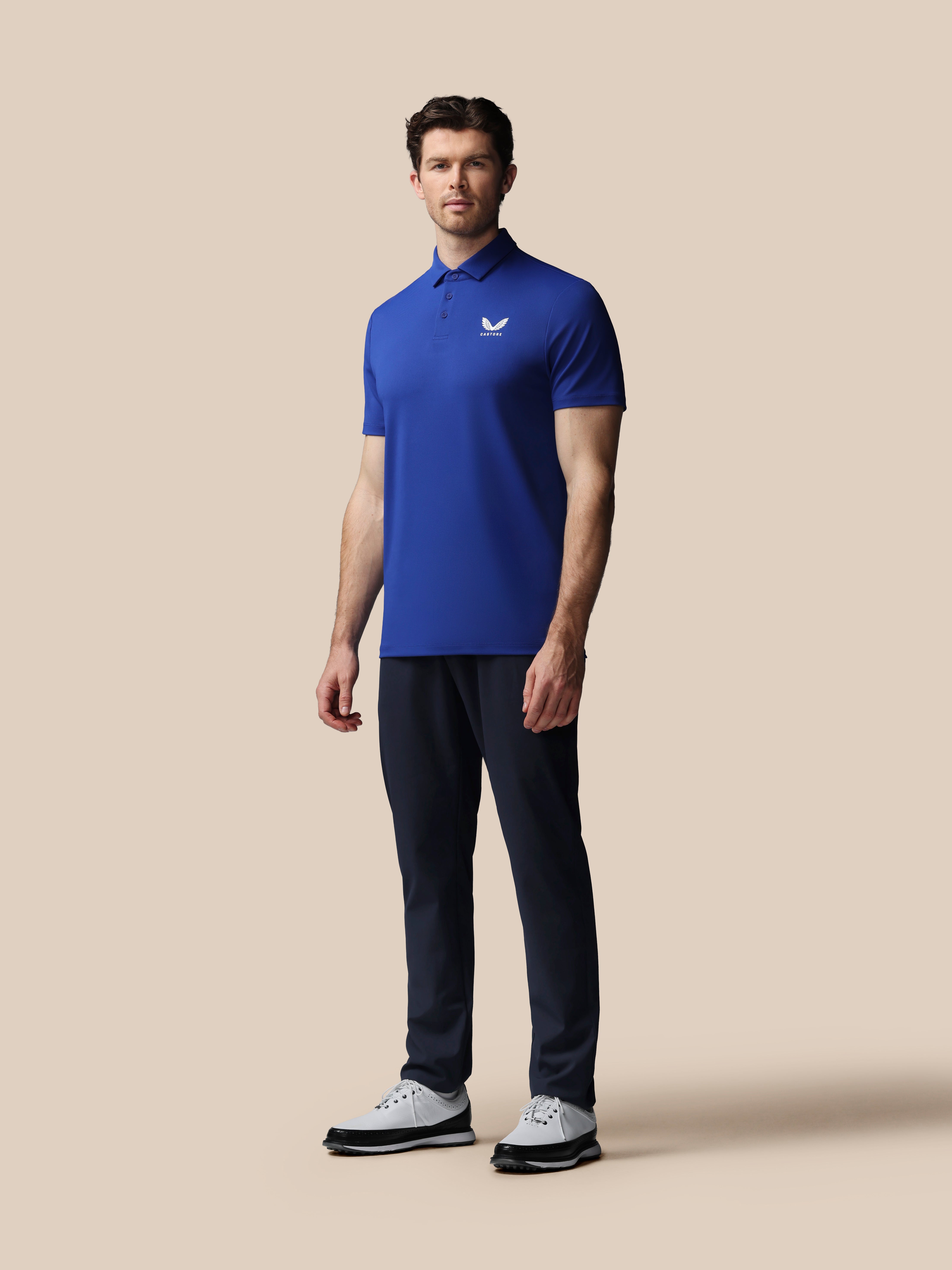 Man wearing a blue polo shirt and dark pants on a beige background