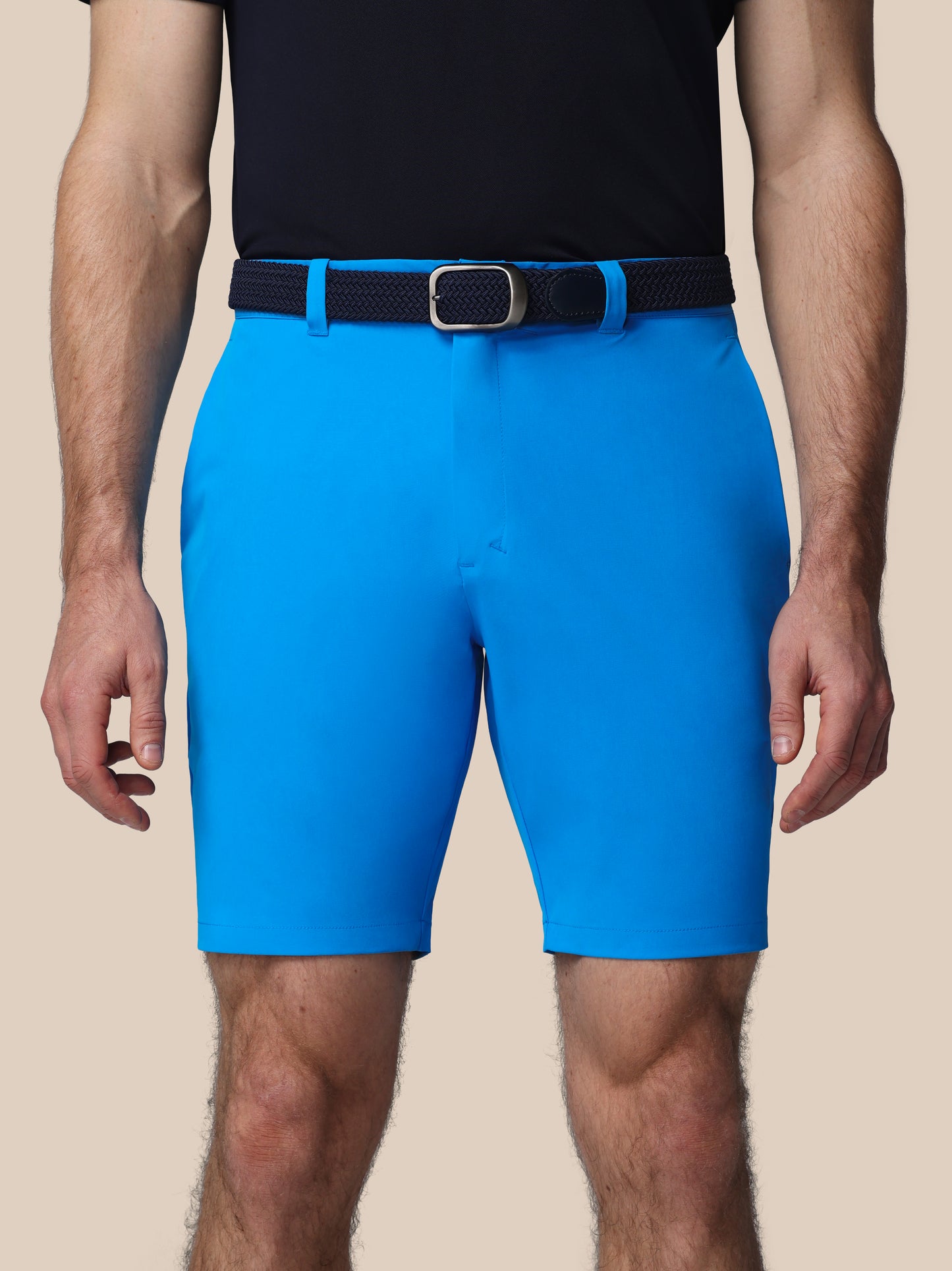 Person wearing bright blue shorts with a black belt on a beige background