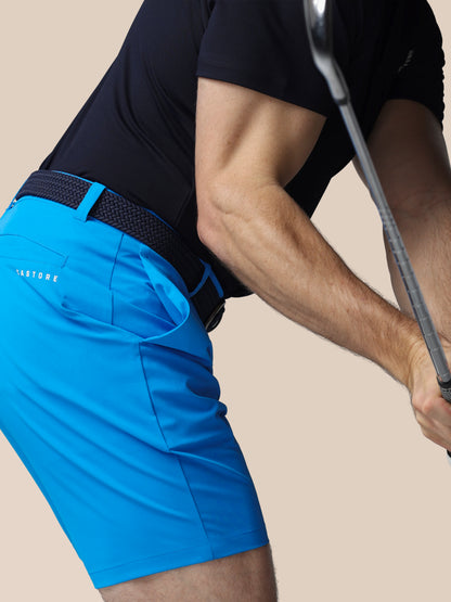 Person wearing blue shorts and black shirt holding a golf club on a beige background