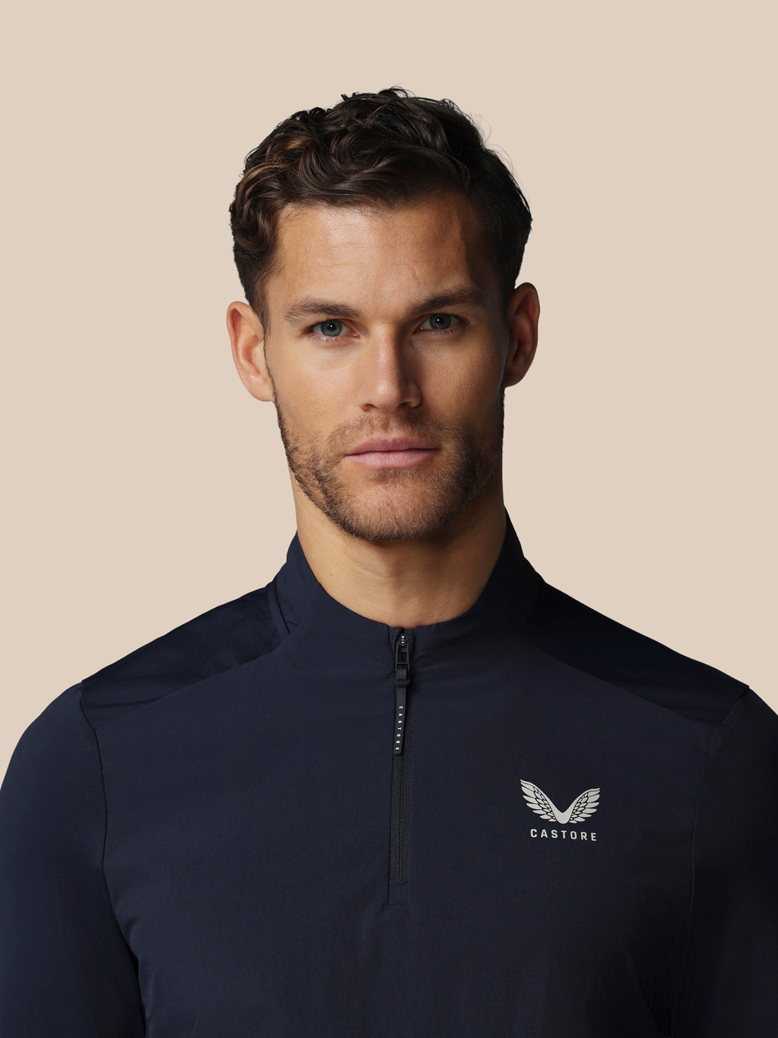 Man wearing a navy blue jacket with a logo on a beige background