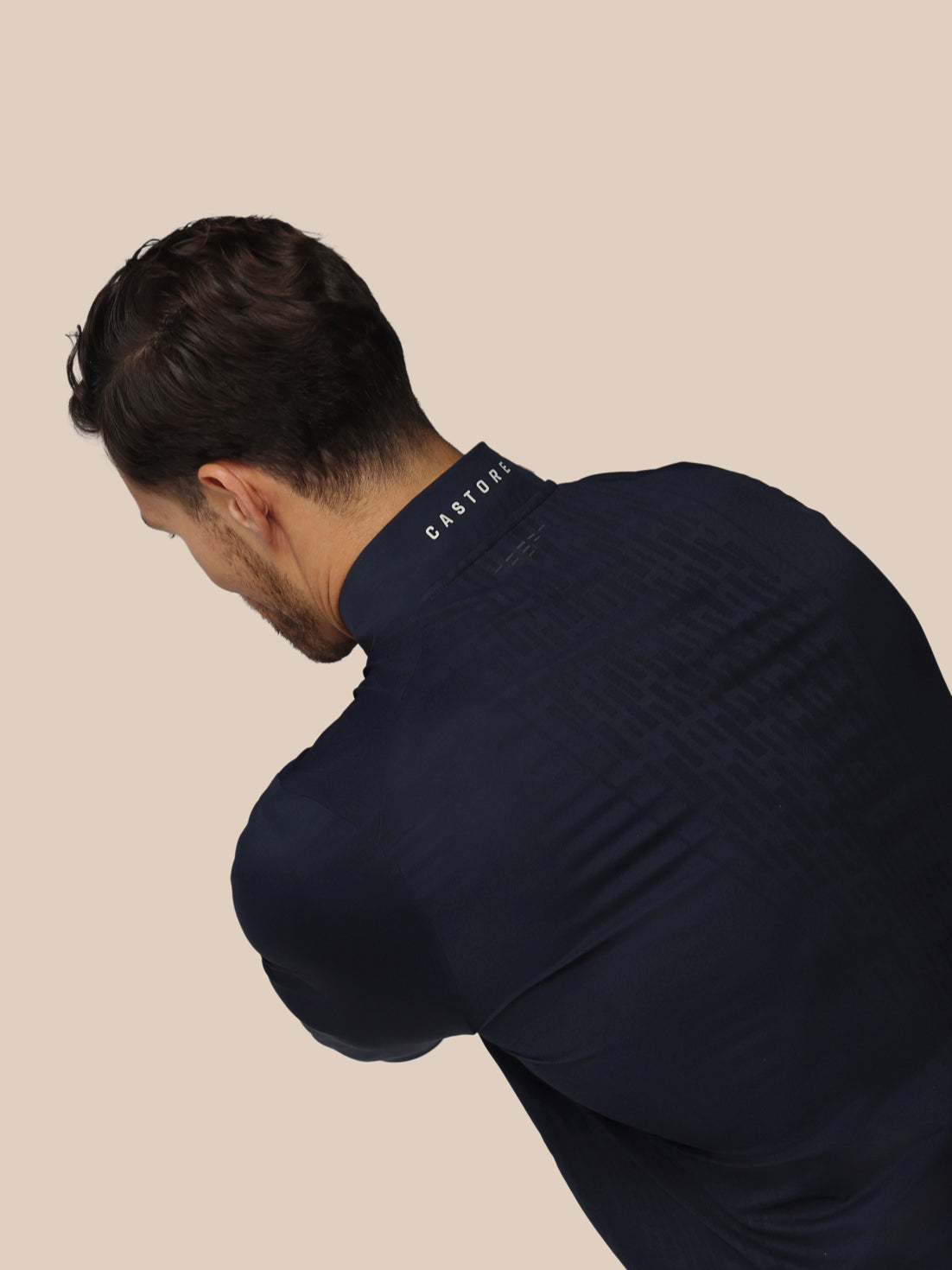 Man wearing a navy blue sweater with 'CASTORE' branding on a beige background