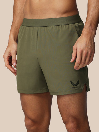 Person wearing green athletic shorts with a brand logo on a beige background