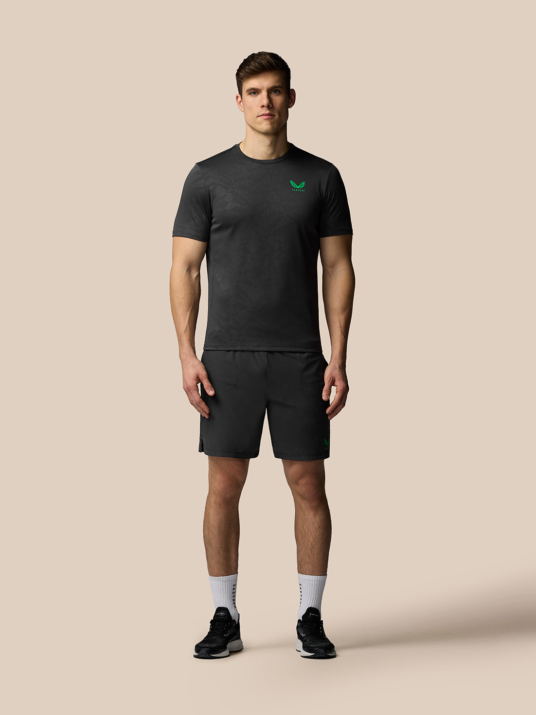 Man wearing a black t-shirt and shorts with a logo on a beige background