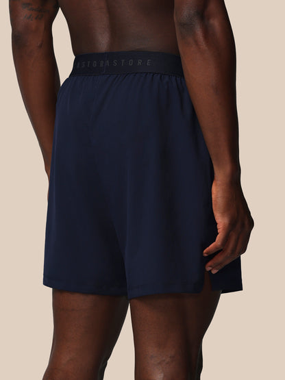 Navy blue athletic shorts with a brand logo on the waistband against a beige background
