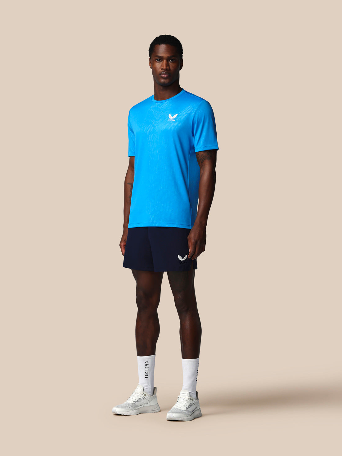 Man wearing a blue athletic shirt and black shorts on a beige background