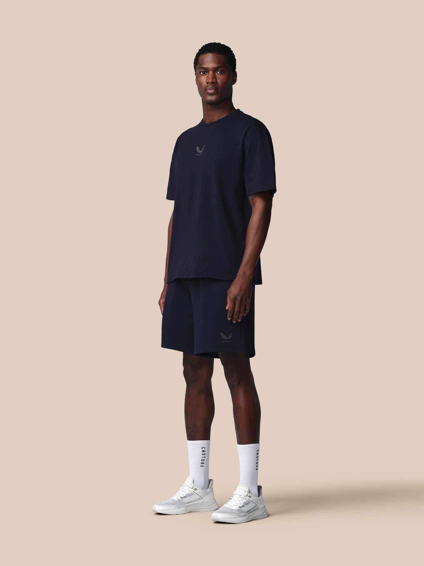 Man wearing a navy blue athletic outfit with white sneakers on a beige background
