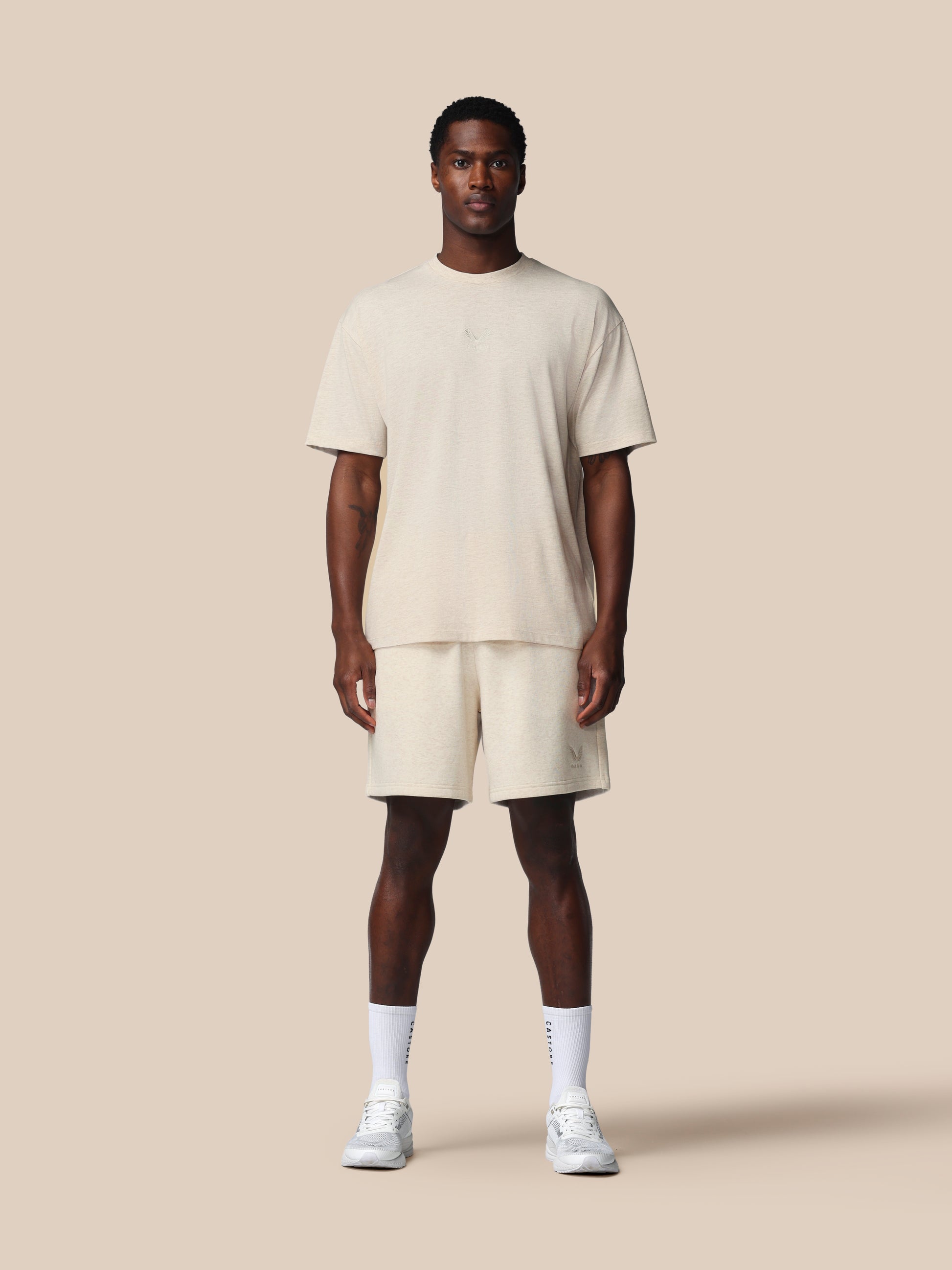 Man wearing a beige t-shirt and shorts set on a plain background