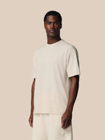 Man wearing a beige t-shirt and pants against a plain background